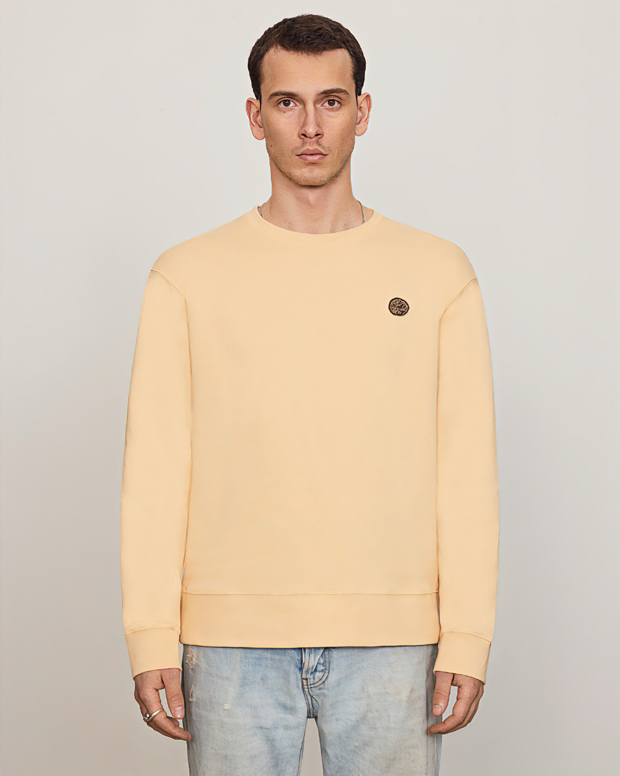 Male model wearing Savoj men’s emblem patch sweatshirt in soft apricot