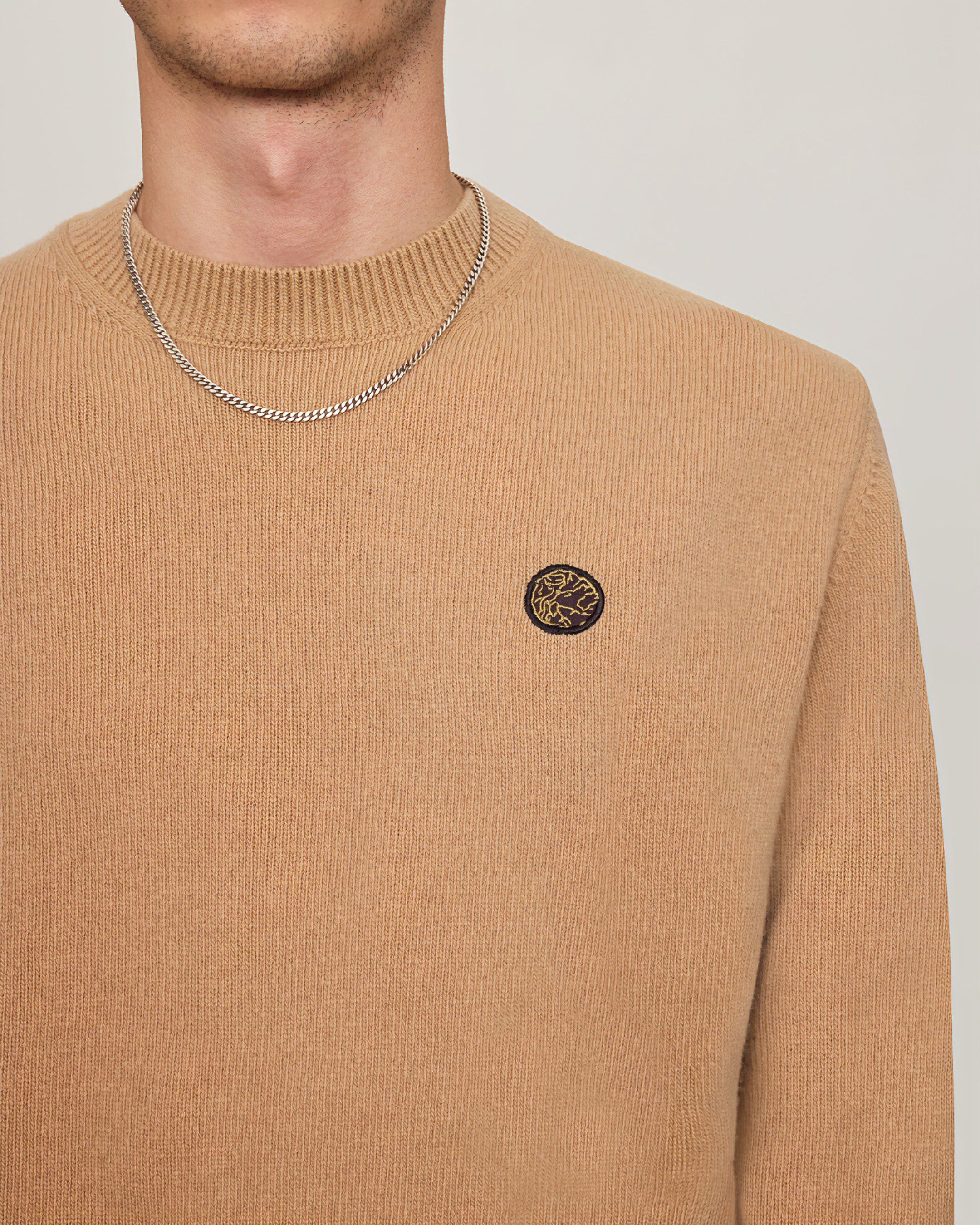 Front view of House of Savoj men's wool sweater in camel beige featuring chest emblem patch